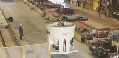A crane operator moves a full concrete bucket from the batch plant to the form.